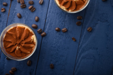 flat lay, Tiramisu two glasses with coffee grains on a blue wooden background. With space for design
