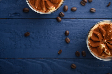 flat lay, Tiramisu two glasses with coffee grains on a blue wooden background. With space for design