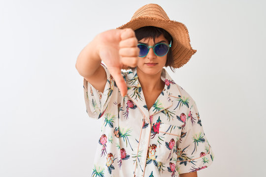 Woman on vacation wearing summer hat shirt and sunglasses over isolated white background with angry face, negative sign showing dislike with thumbs down, rejection concept