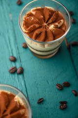 flat lay, Tiramisu two glasses with coffee grains on a green wooden background. vertical photo