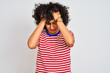 Young arab woman with curly hair wearing striped t-shirt over isolated white background suffering from headache desperate and stressed because pain and migraine. Hands on head.