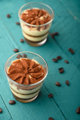 flat lay, Tiramisu two glasses with coffee grains on a green wooden background. vertical photo