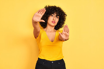 Young arab woman with curly hair wearing t-shirt standing over isolated yellow background doing...