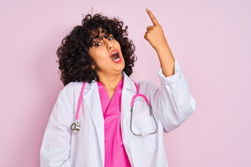 Young arab doctor woman with curly hair wearing stethoscope over isolated pink background pointing finger up with successful idea. Exited and happy. Number one.