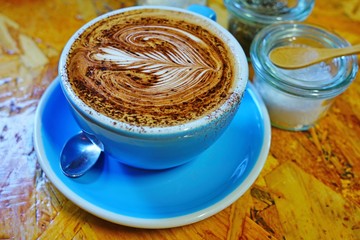 Cup of warm cappuccino coffee with a foam design on top in a blue cup