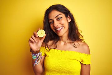 Young beautiful woman holding middle lemon standing over isolated yellow background with a happy face standing and smiling with a confident smile showing teeth