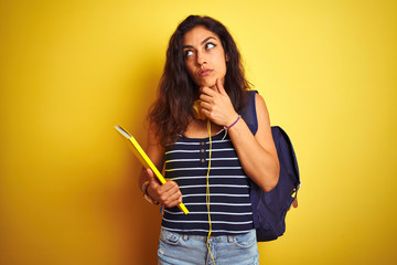 Student woman wearing bakcpack notebook headphones over isolated yellow background serious face thinking about question, very confused idea
