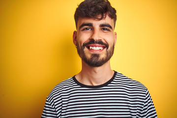 Obraz premium Young man with tattoo wearing striped t-shirt standing over isolated yellow background with a happy and cool smile on face. Lucky person.
