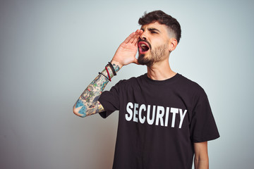 Young safeguard man with tattoo wering security uniform over isolated white background shouting and...
