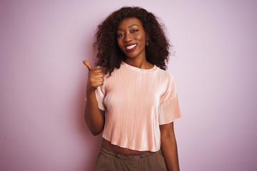 Young african american woman wearing t-shirt standing over isolated pink background doing happy thumbs up gesture with hand. Approving expression looking at the camera showing success.