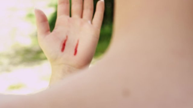 Young girl touching her neck, sees vampire bite tooth marks and red blood marks on her hand. Over shoulder shot from behind.