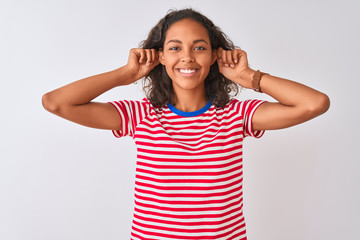 Young brazilian woman wearing red striped t-shirt standing over isolated white background Smiling pulling ears with fingers, funny gesture. Audition problem