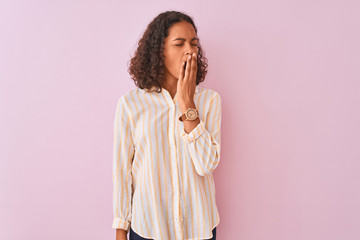 Young brazilian woman wearing striped shirt standing over isolated pink background bored yawning tired covering mouth with hand. Restless and sleepiness.