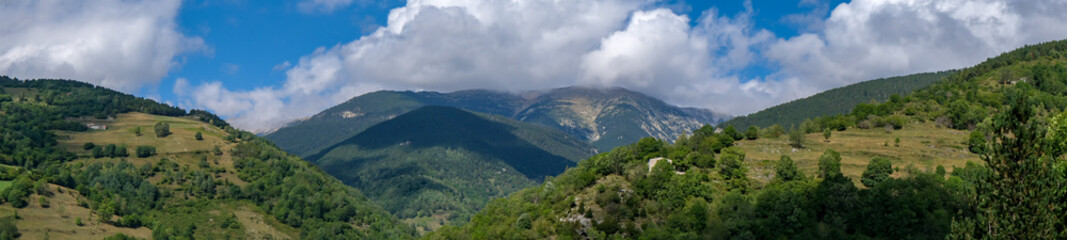 Mountain landscape in Catalonia, Spain. Mountains covered with green trees and shrubs on cloudy blue sky background. Panoramic view, natural background.