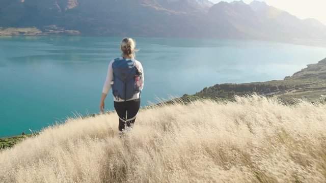 girl hiking in golden grass in New Zealand's mountains over looking blue lake