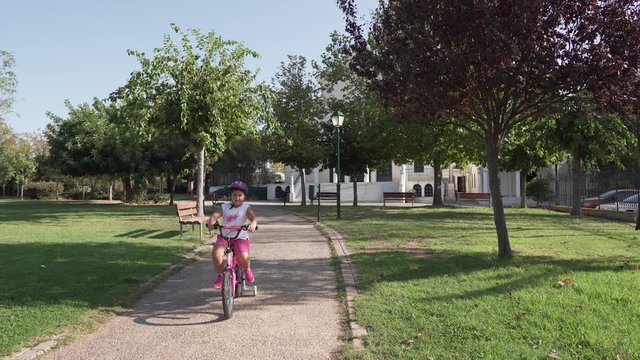 A kid (girl) running down a path in the park with her bicycle.