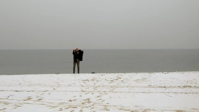 A man puts his winter clothes on on a cold day. Beach in Gdansk Bay.