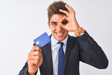 Young handsome businessman wearing suit holding credit card over isolated white background with happy face smiling doing ok sign with hand on eye looking through fingers