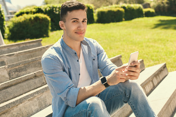 Obraz premium Outdoors Leisure. Stylish guy wearing watch sitting on stairs in park using app on smartphone smiling cheerful close-up