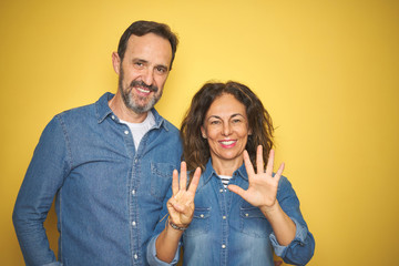 Beautiful middle age couple together standing over isolated yellow background showing and pointing up with fingers number eight while smiling confident and happy.