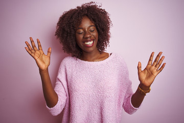 Young african afro woman wearing sweater standing over isolated pink background celebrating mad and crazy for success with arms raised and closed eyes screaming excited. Winner concept