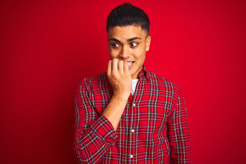 Young brazilian man wearing shirt standing over isolated red background looking stressed and nervous with hands on mouth biting nails. Anxiety problem.