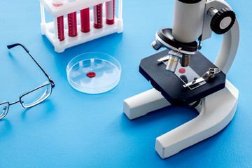 Blood testing laboratory. Samples viewing under microscope near tubes on blue background top view copy space