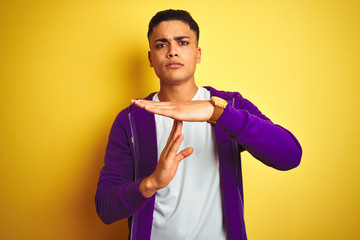Young brazilian man wearing purple sweatshirt standing over isolated yellow background Doing time...