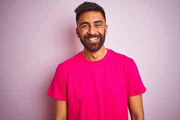 Young indian man wearing t-shirt standing over isolated pink background with a happy and cool smile...