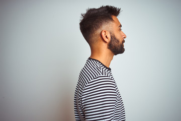 Young indian man wearing black striped t-shirt standing over isolated white background looking to side, relax profile pose with natural face with confident smile.