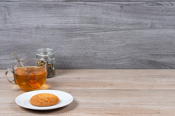 A mug of tea, a jar of tea leaves and a plate of cookies on a background of wooden boards.
