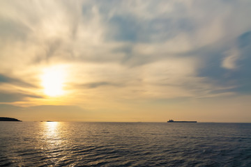 Calm sea with sunset sky and sun through the clouds over