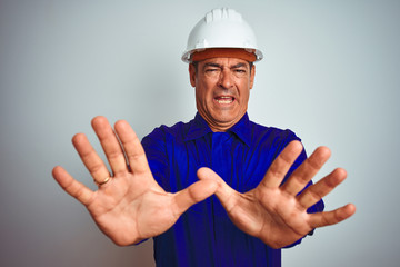 Handsome middle age worker man wearing uniform and helmet over isolated white background afraid and...