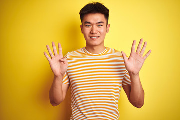 Young asian chinese man wearing t-shirt standing over isolated yellow background showing and pointing up with fingers number nine while smiling confident and happy.
