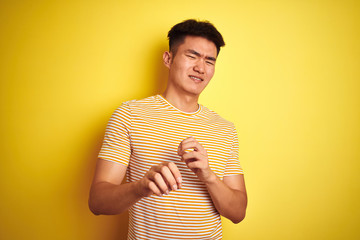 Young asian chinese man wearing t-shirt standing over isolated yellow background disgusted...