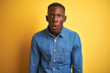 Obraz premium Young african american man wearing denim shirt standing over isolated yellow background afraid and shocked with surprise expression, fear and excited face.