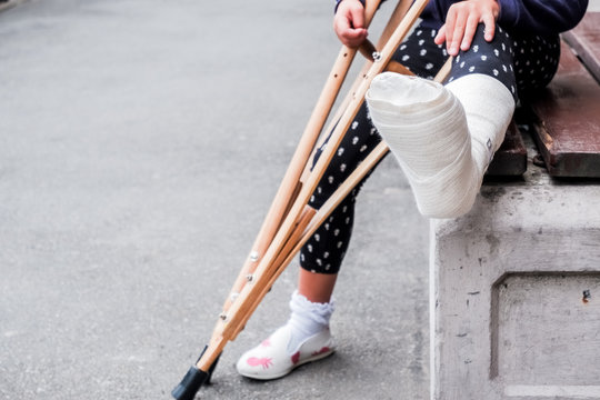 unrecognizable girl sits on the street on a bench with a broken leg and crutches.disabled girl with crutches.an accident while jumping on a trampoline. An ankle fracture.