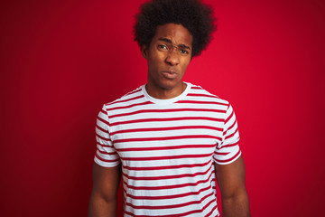 Fototapeta na wymiar Young african american man with afro hair wearing striped t-shirt over isolated red background depressed and worry for distress, crying angry and afraid. Sad expression.