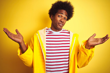 African american man with afro hair wearing rain coat standing over isolated yellow background...