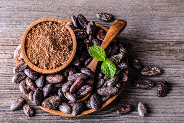 Cocoa beans and powder in wooden bowl spoon on old rustic background.