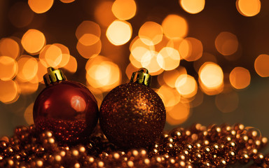 Two Christmas ornaments lying on balls of a Christmas chain on a blurred background with lights.