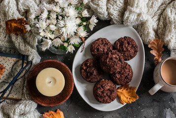 Chocolate cakes with almonds, coffee, knitted plaid, book, bouquet of chrysanthemums, candle on a dark background, top view