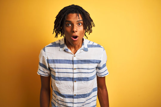 Afro american man with dreadlocks wearing striped shirt over isolated yellow background afraid and shocked with surprise expression, fear and excited face.