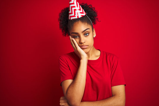 Young afro american woman wearing birthday hat over isolated red background thinking looking tired and bored with depression problems with crossed arms.