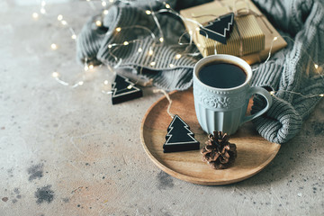 Christmas background with mug of hot coffee, cozy sweater, garland lights, gifts and festive decoration. Copy space for text. Cozy mood holiday card concept.