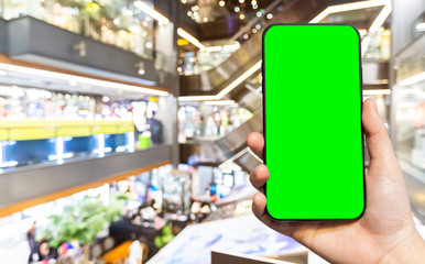 Fototapeta premium Close-up of female use Hand holding smartphone with empty blank green screen blurred images touch of Abstract blur of inside shopping complex background,shopping online concept.