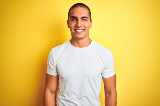 Young caucasian man wearing casual white t-shirt over yellow isolated background winking looking at the camera with sexy expression, cheerful and happy face.