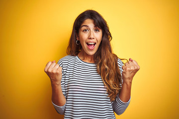 Young beautiful woman wearing stripes t-shirt standing over yelllow isolated background celebrating surprised and amazed for success with arms raised and open eyes. Winner concept.