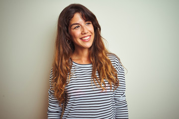 Young beautiful woman wearing stripes t-shirt over white isolated background looking away to side with smile on face, natural expression. Laughing confident.