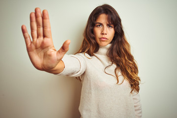 Young beautiful woman wearing winter sweater standing over white isolated background doing stop sing with palm of the hand. Warning expression with negative and serious gesture on the face.